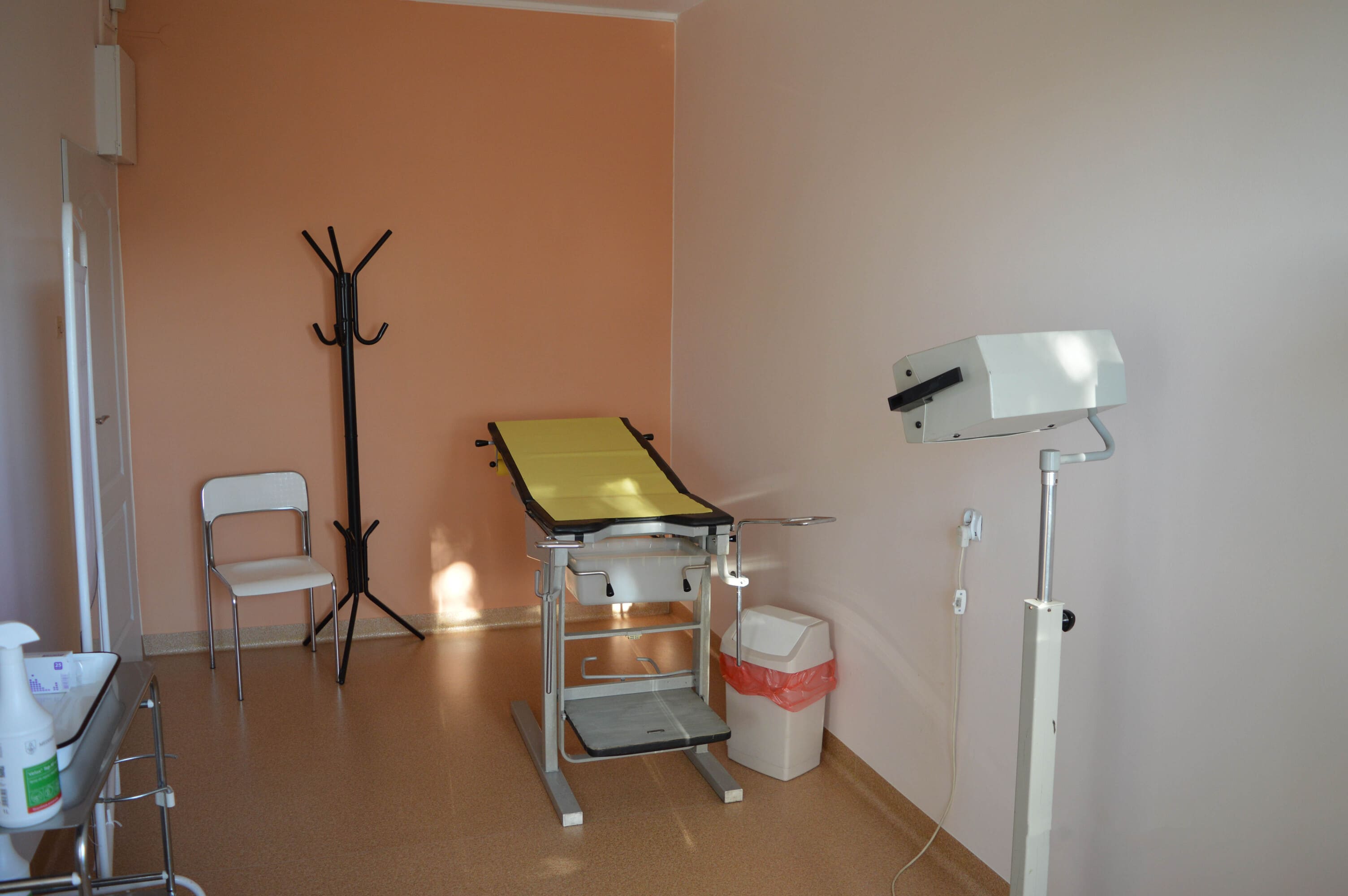 Gabinet ginekologiczny, w części centralnej  widoczna leżanka w kolorze żółtym oraz lampa na podnośniku.
